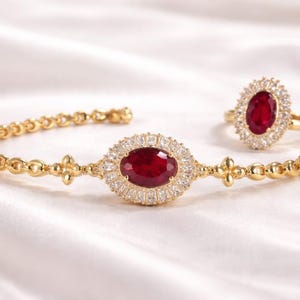 Peut inclure: Un ensemble de bijoux en or, composé d'un bracelet et d'une bague. Le bracelet présente un rubis central ovale entouré de diamants, avec une bague assortie. L'ensemble est sur fond blanc.