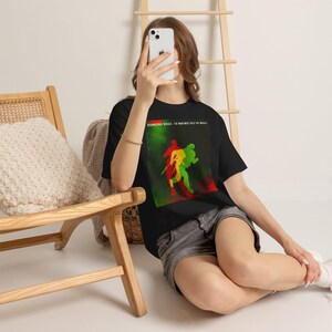 May include: A black short-sleeve t-shirt featuring a graphic print with red, yellow, and green silhouettes of figures. The text "DIAMOND DOGS" and "THE MAN WHO SOLD THE WORLD" is printed in white at the top of the rectangular graphic design.