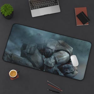 May include: A rectangular mouse pad featuring a detailed illustration of a futuristic soldier in a battle scene. The design incorporates shades of gray, blue, and white, with a black border. A white computer mouse rests on the pad.