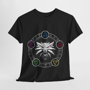 Op de afbeelding: Zwart t-shirt met een wit wolfskop-embleem met rode ogen, omringd door een cirkelvormig ontwerp met kleurrijke geometrische symbolen. Het ontwerp is gecentreerd op de voorkant.