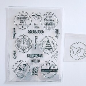 May include: A clear plastic Christmas stamp set with festive designs and text. The set includes stamps with phrases such as "Merry Christmas" and "Happy New Year." Designs include a Christmas tree, clock, and bear. A separate die-cut set is also included.