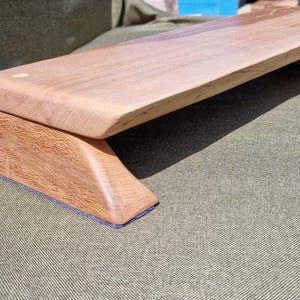 May include: A rectangular wooden monitor stand featuring a light-coloured, smooth top surface with rounded edges and two sturdy, darker-toned wooden support legs. The stand has a clean, natural wood grain finish and a simple, elevated design.
