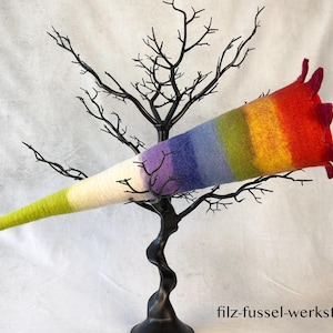 Puede incluir: Una escultura en forma de cuerno afieltrado en colores del arcoíris, del verde al rojo, se exhibe en un árbol de metal negro. La escultura tiene una base blanca y está adornada con el texto "filz-fussel-werkstatt.de".