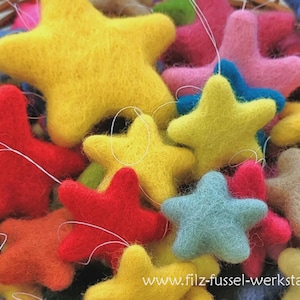 Op de afbeelding: Een close-up van een verzameling kleurrijke vilten sterornamenten in geel, rood, roze, blauw en oranje. Elke ster heeft een wit touwtje om op te hangen. De handgemaakte decoraties zijn in verschillende tinten.