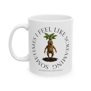 Könnte beinhalten: Weiße Keramik-Tasse mit umlaufendem Design mit einer Illustration einer schreienden Alraune. Der Text "SOMETIMES I FEEL LIKE SCREAMING" umrundet das Bild, darunter "MANDRAGORA OFFICINALIS".