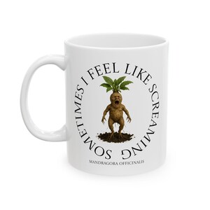 Könnte beinhalten: Weiße Keramiktasse mit einem umlaufenden Design, das eine Illustration einer schreienden Alraune zeigt. Der Text "SOMETIMES I FEEL LIKE SCREAMING" umkreist das Bild, darunter "MANDRAGORA OFFICINALIS". Die Tasse hat einen weißen Henkel.