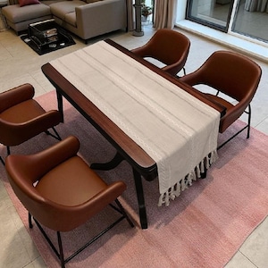 May include: A dining room set featuring a dark wood table with a cream-colored runner and four brown leather chairs. The chairs have black metal legs. The set is placed on a pink rug.