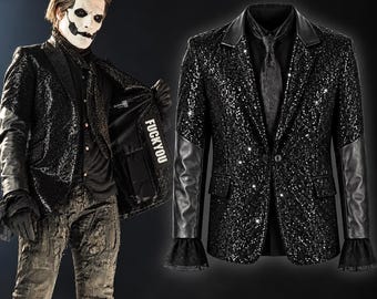 May include: A black sequined blazer featuring smooth leather sleeves, a notched lapel, and a single-button closure. The interior lining displays the text FUCKYOU in white lettering. The garment is paired with a black shirt and a black necktie.