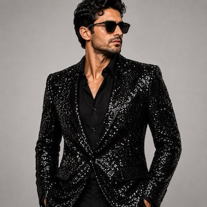 Può includere: Un blazer nero con paillettes indossato sopra una camicia nera abbottonata. Il blazer presenta un classico design a revers ed è interamente ricoperto di paillettes nere scintillanti. L'insieme è completato da occhiali da sole neri.