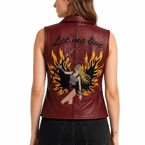 May include: A sleeveless burgundy leather waistcoat featuring an embroidered graphic on the back. The design depicts a warrior figure holding a spear, surrounded by yellow and black flames, with the text Let me live embroidered in black script above.