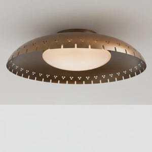 May include: A bronze-coloured, mid-century modern ceiling light fixture. The fixture has a rounded, saucer-like shape with a perforated edge and a central, frosted glass diffuser. The light is designed to be mounted flush against the ceiling.
