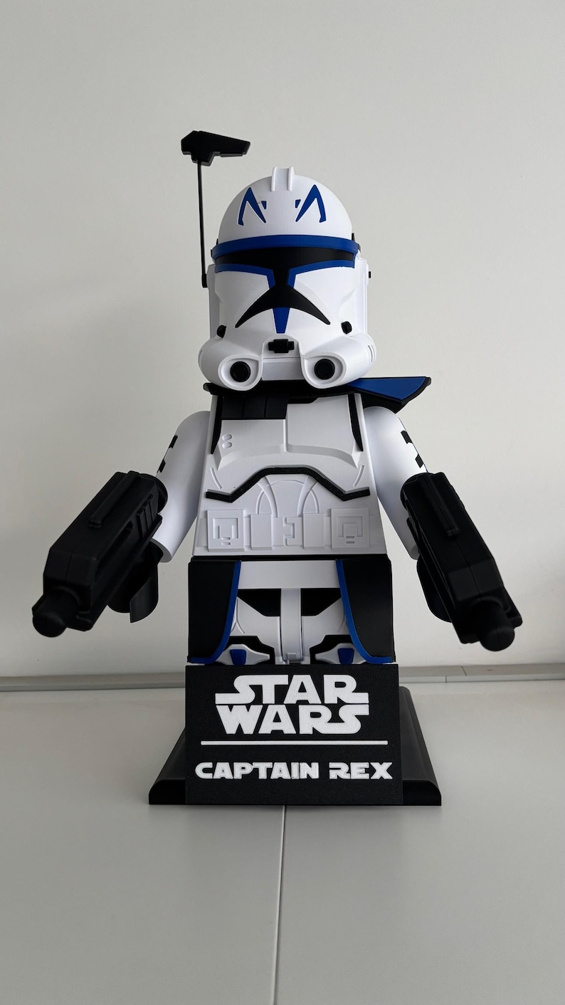 May include: A large Captain Rex figure in white and blue, from Star Wars. The figure has a black base with the Star Wars logo and Captain Rex text. It features black blasters and a helmet with blue markings.