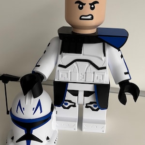 May include: A large, white and blue clone trooper action figure with a matching helmet. The figure has a bald head with an angry expression, black accents, and blue shoulder pads. The helmet is held in the left hand.