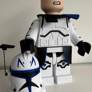 May include: A large white and blue figurine of a character with a helmet and a separate helmet. The figurine has a bald head with an angry expression. The helmet is white with blue accents. The figurine is in a standing position.