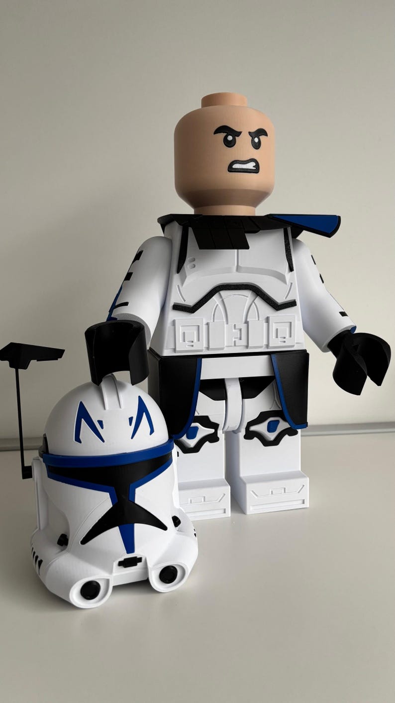 May include: A large white and blue figurine of a character with a helmet and a separate helmet. The figurine has a bald head with an angry expression. The helmet is white with blue accents. The figurine is in a standing position.
