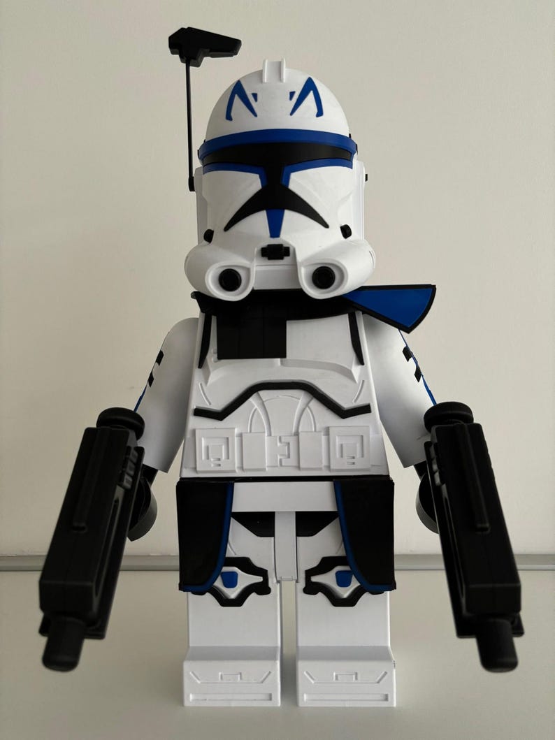 May include: A white and blue clone trooper action figure with black blasters. The figure has a helmet with blue markings and a black antenna. The armour is white with black and blue accents.