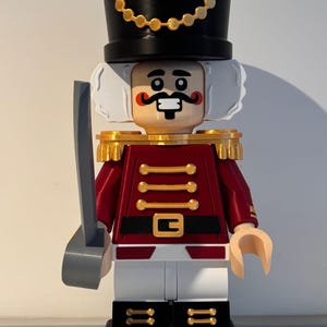 Op de afbeelding: Een decoratief kerstnotenkrakerbeeldje in de stijl van een bouwsteenspeelgoed. De figuur is rood, zwart en goudkleurig en houdt een zwaard vast. De basis luidt "MERRY CHRISTMAS".