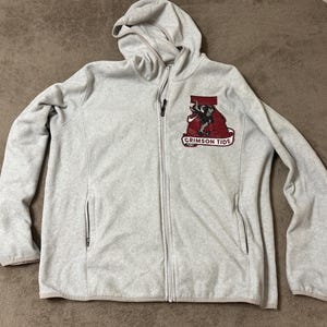 May include: A light gray zip-up hoodie with a hood and two front pockets. The hoodie features a red and black graphic of an elephant and the words "CRIMSON TIDE" on the chest.