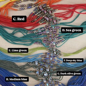 May include: A selection of beaded bracelets in various colours, each featuring a central decorative piece. The bracelets are displayed in a fan arrangement, with colours such as yellow, orange, red, sea green, lime green, deep sky blue, dark olive green, medium blue, and midnight blue.