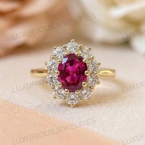 Könnte beinhalten: Ein goldener Ring mit einem zentralen ovalen Rubin, umgeben von einem Kranz aus kleineren Diamanten. Der Ring hat ein schlichtes Goldband. Der Text "LUXURIOUSJEWELRIES" ist auf dem Bild abgebildet.