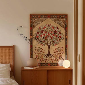 May include: A framed wall art piece featuring a tree with red fruit, set against a beige backdrop. The artwork has a decorative border with floral patterns in red, brown, and gold. The art is displayed above a wooden cabinet with a round vase and a small lamp.