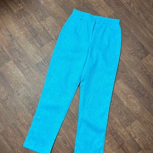 May include: Bright turquoise high-waisted trousers featuring a subtle snakeskin texture pattern throughout. The trousers include a front zip fly, a single button fastening at the waistband, and belt loops. The legs are straight and full-length.