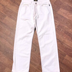 May include: A pair of off-white denim jeans. The jeans have a classic five-pocket design, a button and zipper closure, and a straight leg fit. The jeans are made of a medium-weight denim fabric.