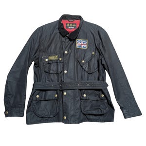 Peut inclure: Une veste cirée noire Barbour International avec un col en velours côtelé, une ceinture à la taille et quatre poches avant à boutons-pression en laiton. La poitrine porte un écusson Barbour International et un drapeau Union Jack avec Barbour.