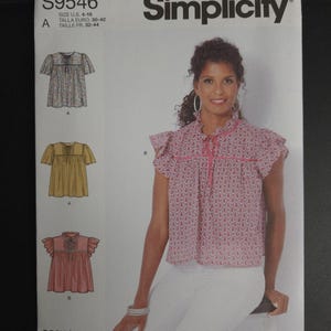 May include: Simplicity sewing pattern S9546 featuring a woman wearing a pink patterned top. The pattern includes illustrations of three different blouse designs. The text "easy-to-sew" is printed on the bottom of the pattern.