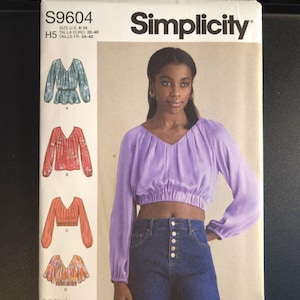 May include: Simplicity sewing pattern S9604 featuring a woman wearing a purple crop top and jeans. The pattern includes illustrations of different blouse styles. The text "easy-to-sew" is visible.