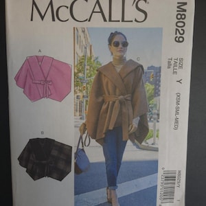 May include: McCall's sewing pattern M8029 featuring a hooded cape with a tie closure. The pattern includes illustrations of the cape in pink and black plaid. The cover shows a woman wearing the cape in a neutral color.