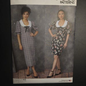 May include: Vogue Patterns sewing pattern V1905. The pattern features two dress designs with white collars. One dress is a gray plaid, and the other is black with a floral print. The pattern is designed and printed in the USA.