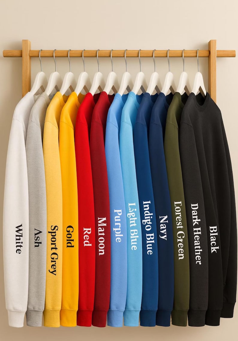 May include: A display of crewneck sweatshirts in various colors, including white, ash, sport grey, gold, red, maroon, purple, light blue, indigo blue, navy, forest green, dark heather, and black. Each sweatshirt hangs on a wooden rack.