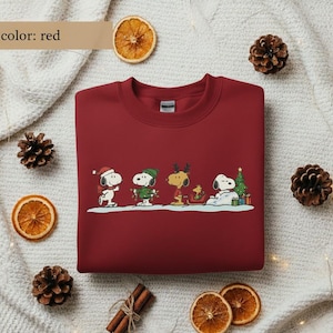 May include: A red crewneck sweatshirt featuring a festive Snoopy and friends design. The graphic includes Snoopy, Woodstock, and other Peanuts characters in holiday attire, with a Christmas tree and gifts. The text "color: red" is in the upper left corner.