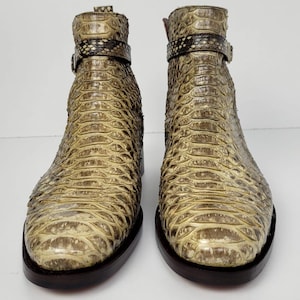 Puede incluir: Un par de botines con estampado de piel de serpiente en tonos beige y marr&oacute;n. Los botines tienen suela marr&oacute;n oscuro y una correa con hebilla alrededor del tobillo. Los botines est&aacute;n hechos de un material texturizado.