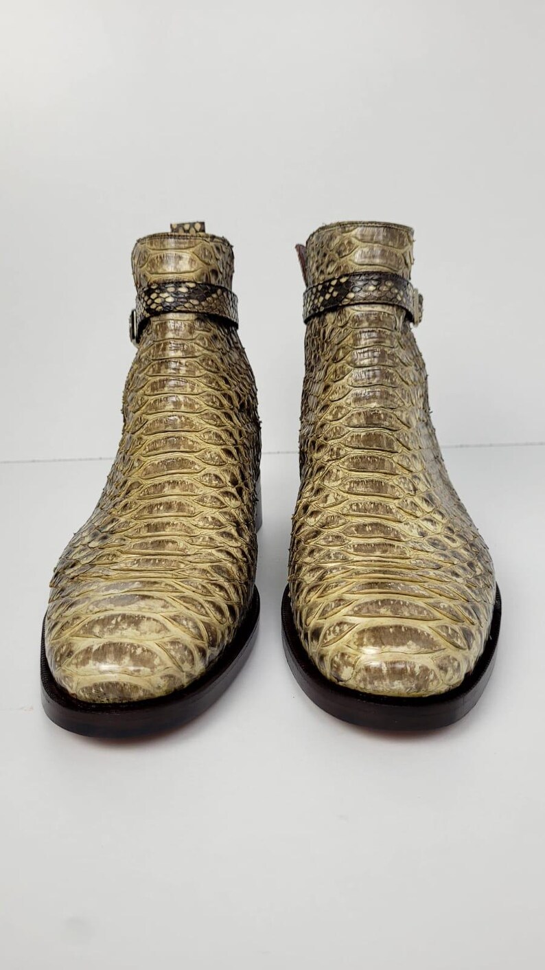 Puede incluir: Un par de botines con estampado de piel de serpiente en tonos beige y marr&oacute;n. Los botines tienen suela marr&oacute;n oscuro y una correa con hebilla alrededor del tobillo. Los botines est&aacute;n hechos de un material texturizado.