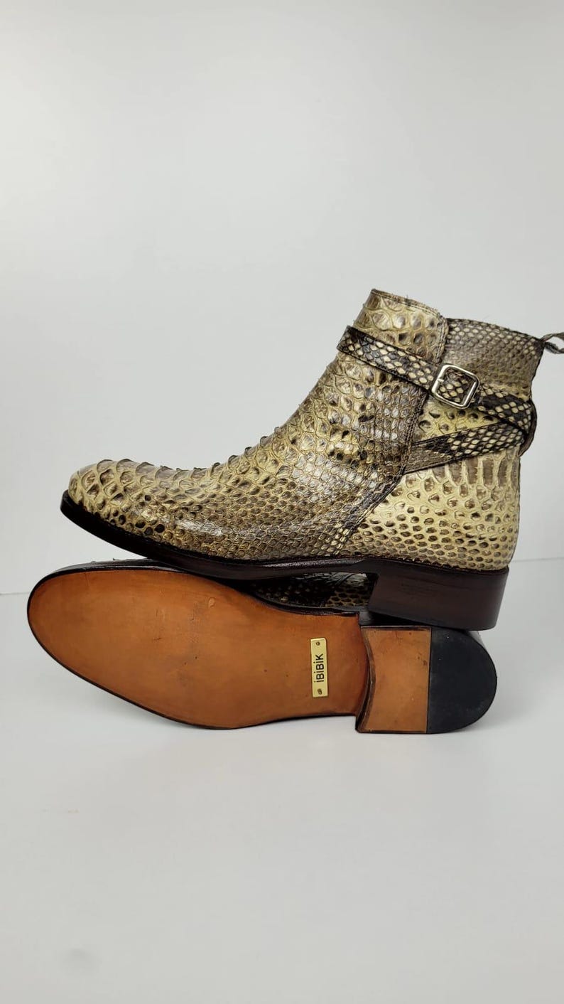 Puede incluir: Botines con estampado de piel de serpiente en tonos beige, marr&oacute;n y negro. Las botas tienen cierre de hebilla y suela de cuero. Se ve la suela de una bota, con la marca "IBIBIK".