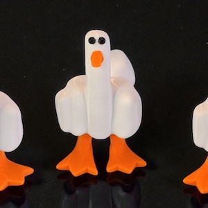 May include: Three white goose figurines with orange feet and beaks. The geese are standing on a reflective black surface. These novelty ornaments would make a fun addition to a home or office.