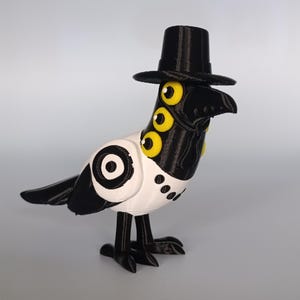 Puede incluir: Una caprichosa figura de p&aacute;jaro en blanco y negro con sombrero de copa. El p&aacute;jaro tiene m&uacute;ltiples ojos amarillos y un pico negro. El cuerpo es blanco con detalles negros y un dise&ntilde;o circular. La figura est&aacute; sobre una superficie gris claro.