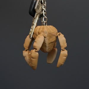 May include: A wooden articulated figure keyring with a key ring and keys. The figure is light brown and has a rounded head and jointed limbs. The background is a solid dark grey.