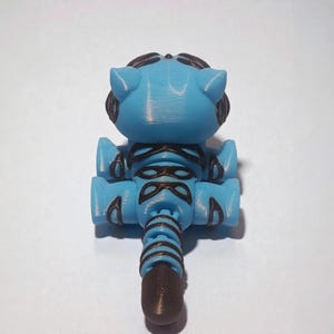 Puede incluir: Un juguete robot azul y marr&oacute;n impreso en 3D. El robot tiene una cabeza redondeada con orejas, una cara detallada y un cuerpo segmentado. El juguete est&aacute; hecho de pl&aacute;stico y tiene una textura suave.