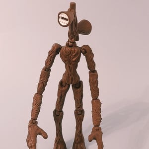 Op de afbeelding: Een bruin Siren Head actiefiguur met een luidsprekerachtige kop en beweegbare ledematen. Het figuur heeft een gedetailleerd, getextureerd ontwerp en staat op een effen achtergrond. De mond is open en toont witte tanden.