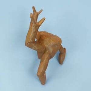 Pode incluir: Escultura impressa em 3D de uma figura humana em pose din&acirc;mica, com os bra&ccedil;os levantados e as pernas estendidas. A figura &eacute; de cor castanha clara e parece ser feita de pl&aacute;stico. O fundo &eacute; azul claro s&oacute;lido.
