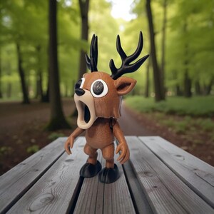 May include: A brown deer figurine with black antlers, large white eyes, and an open mouth. The figurine has small arms and black feet. It is standing on a wooden table with a blurred forest background.