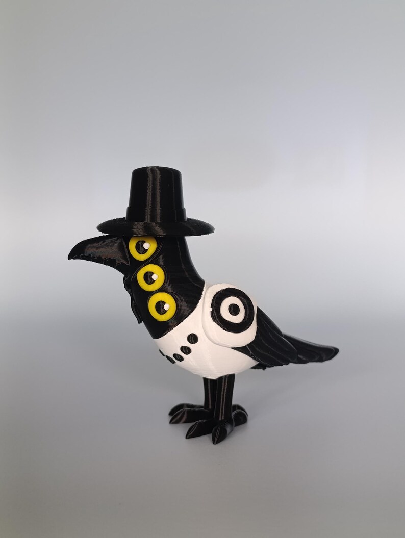 Puede incluir: Una figura de cuervo impresa en 3D en blanco y negro, con un sombrero de copa negro. El cuervo tiene tres ojos amarillos y un pecho blanco con puntos negros. El p&aacute;jaro est&aacute; de pie sobre dos patas negras.