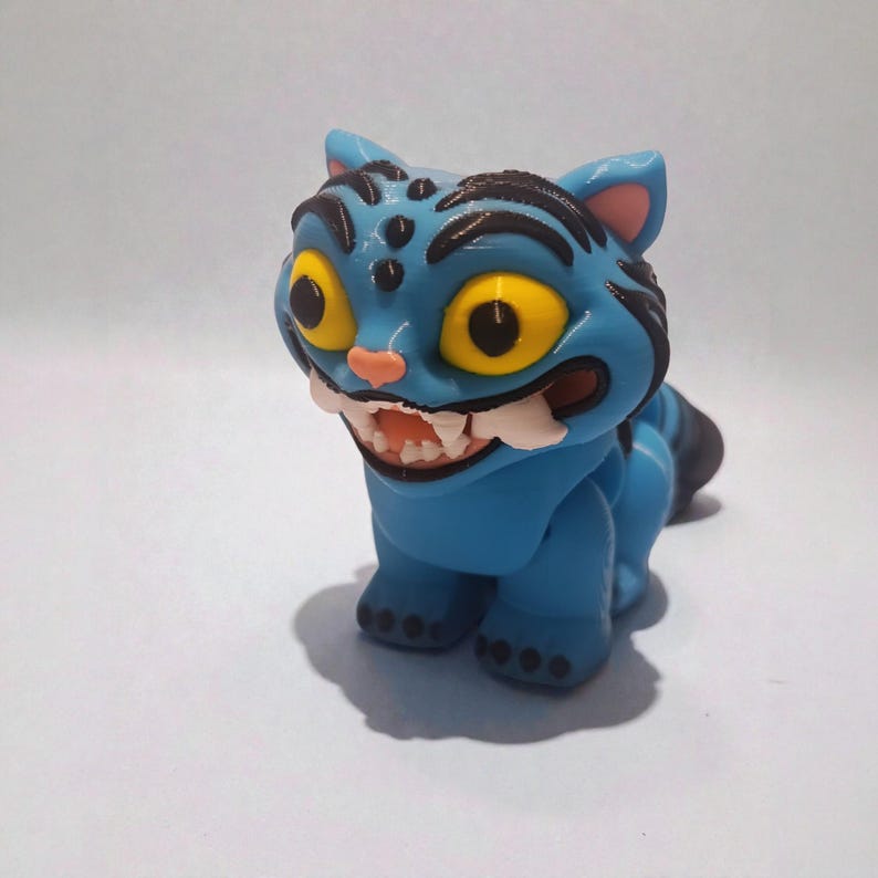 Puede incluir: Figura de gato azul con ojos amarillos y una amplia sonrisa con dientes. El gato tiene rayas negras y una nariz y orejas rosas. Este coleccionable caprichoso es un art&iacute;culo decorativo &uacute;nico.