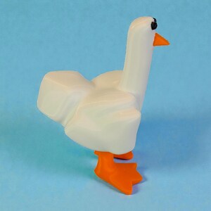 May include: A white goose figurine with orange feet and beak, and black eyes. The goose is standing on a light blue surface. The figurine has a smooth, glossy finish and is a whimsical decorative item.
