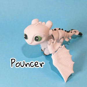 May include: A white dragon figurine with green eyes and black accents on its back and tail. The dragon has large wings and is posed on a blue background. The word "Pouncer" is written in a white font with a black outline.