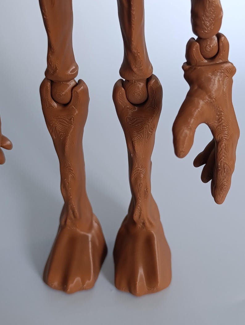 May include: A close-up of a brown, articulated model of a creature's legs and hand. The legs have hoof-like feet and detailed joint structures. The hand is open, with fingers slightly curved.