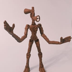 Op de afbeelding: Een bruin Siren Head actiefiguur met beweegbare gewrichten. De figuur heeft een uniek ontwerp, met een hoofd in de vorm van een paar luidsprekers en lange armen. De figuur poseert met uitgestrekte armen, waarbij het gedetailleerde, getextureerde oppervlak wordt getoond.